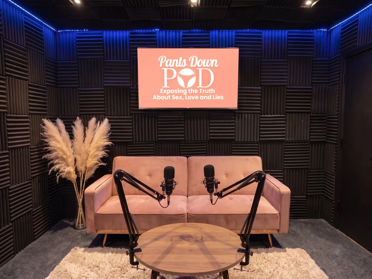 A pink sofa with two microphones on boom arms, Pants Down Pod artwork on the screen