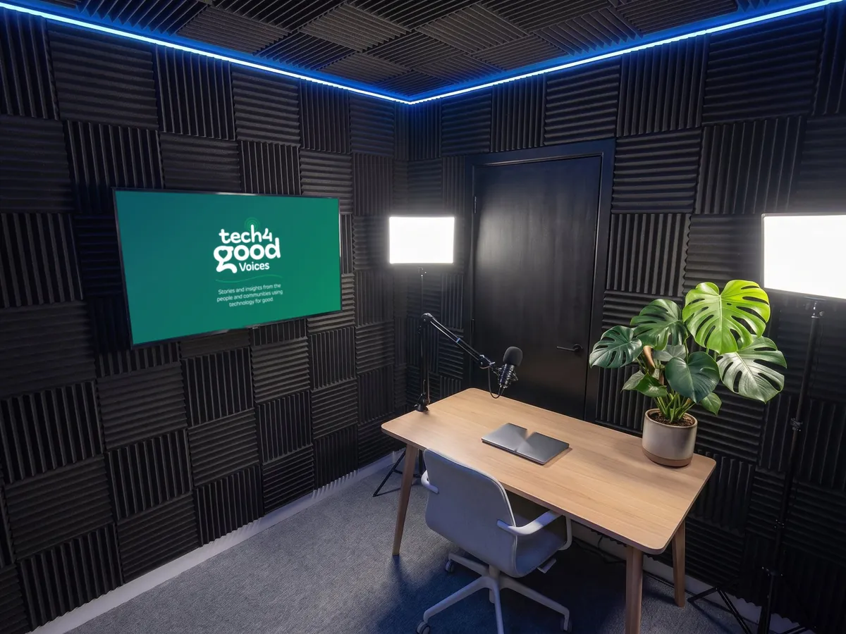 A solo presenter desk with a plant and two LED panels, Tech 4 Good Voices artwork on the screen