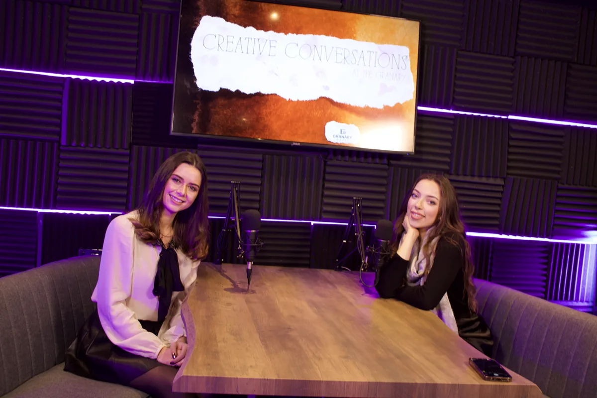 Creative Conversations recording in the Granary podcast studio: two hosts at the live-edge table under purple LED light